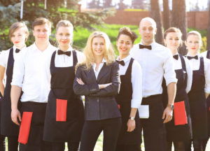 A large group of waiters and waitresses in the open air stand one after another on a sunny day